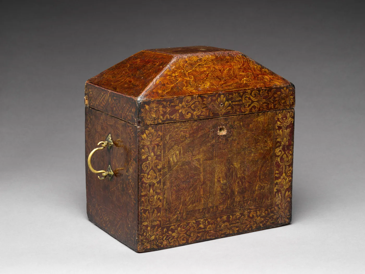 Small Chinese lacquer chest with a sloping lid, brass handles and fine gold decoration over a dark red-brown ground that is worn at the edges