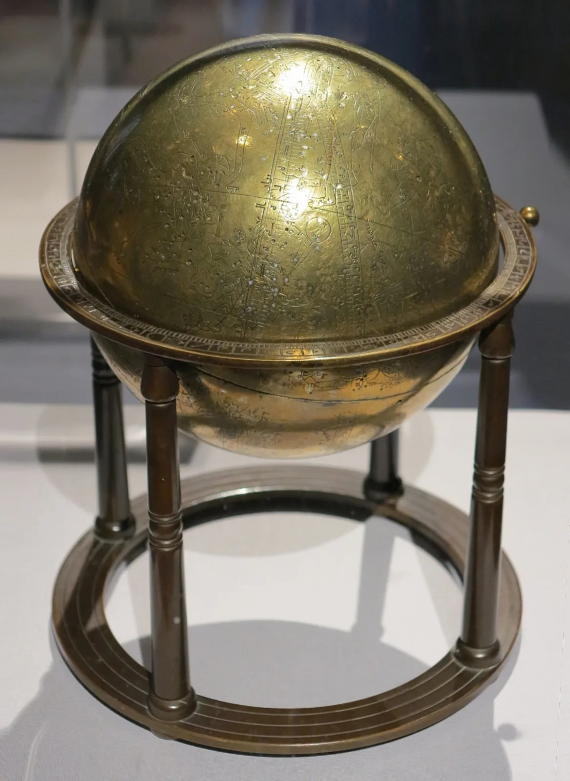 Brass celestial globe engraved and inlaid with silver constellation figures and star points, resting in a plain brass ring stand