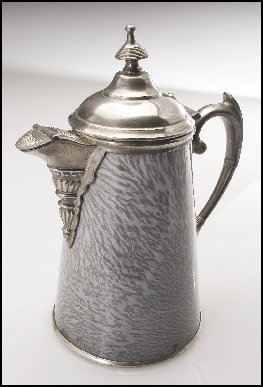 Tapered coffeepot with a grey streaked enamel body and bright pewter mounts: a domed hinged lid with turned finial, an ornate cast spout mount and a shaped pewter handle