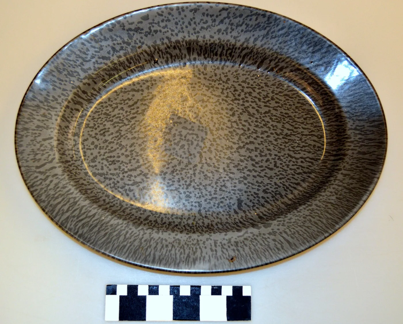 Large oval platter, its surface covered edge to edge in fine dark speckles over a paler grey ground, with a scale bar below