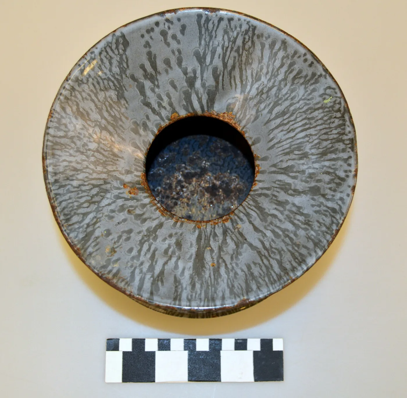 Spittoon photographed from directly above, its grey mottled enamel radiating from a central hole, with orange rust breaking through around the opening and along the outer rim