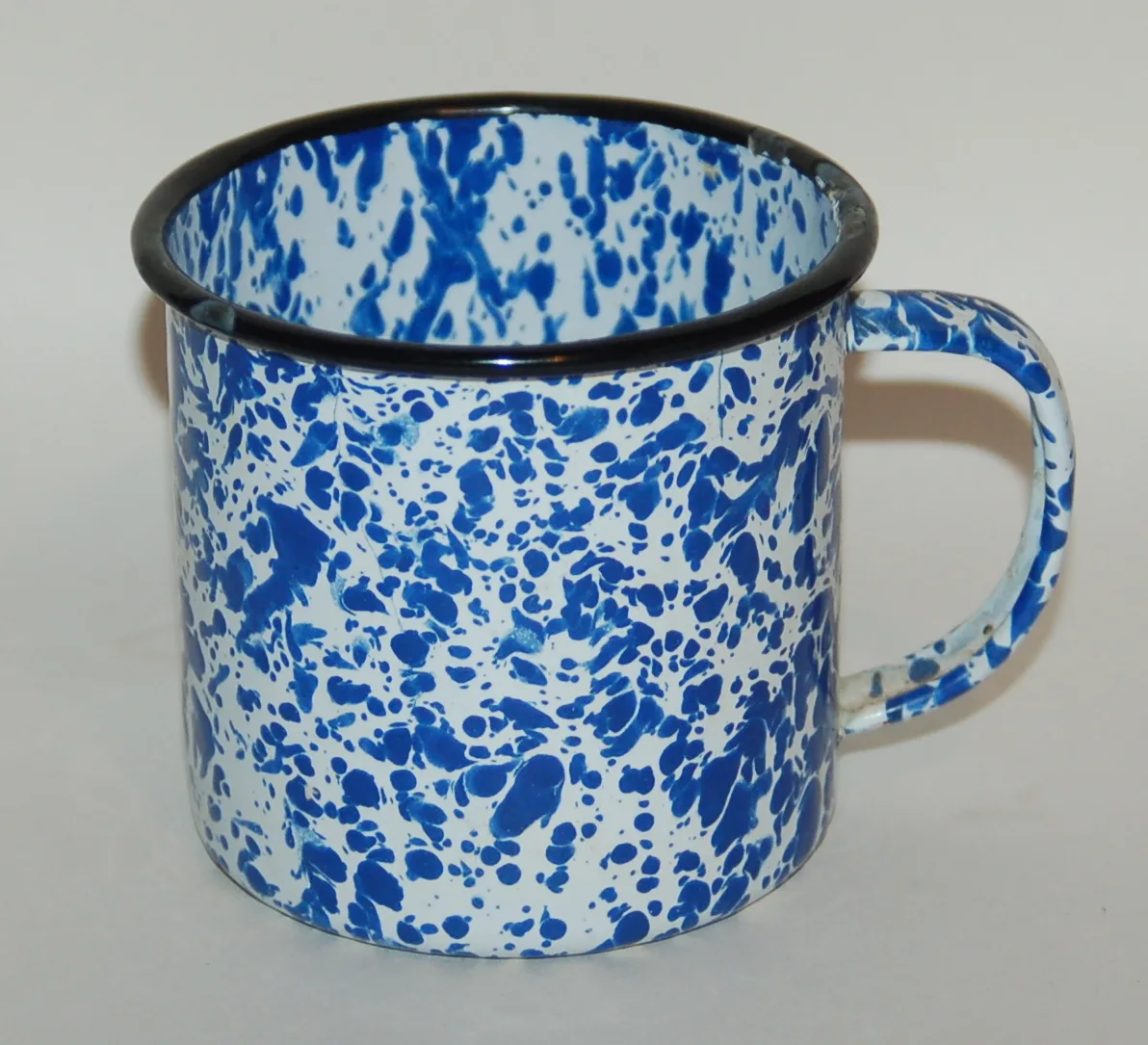 Straight-sided mug with a white enamel ground heavily spattered in deep blue, finished with a black rolled rim and a matching spattered handle