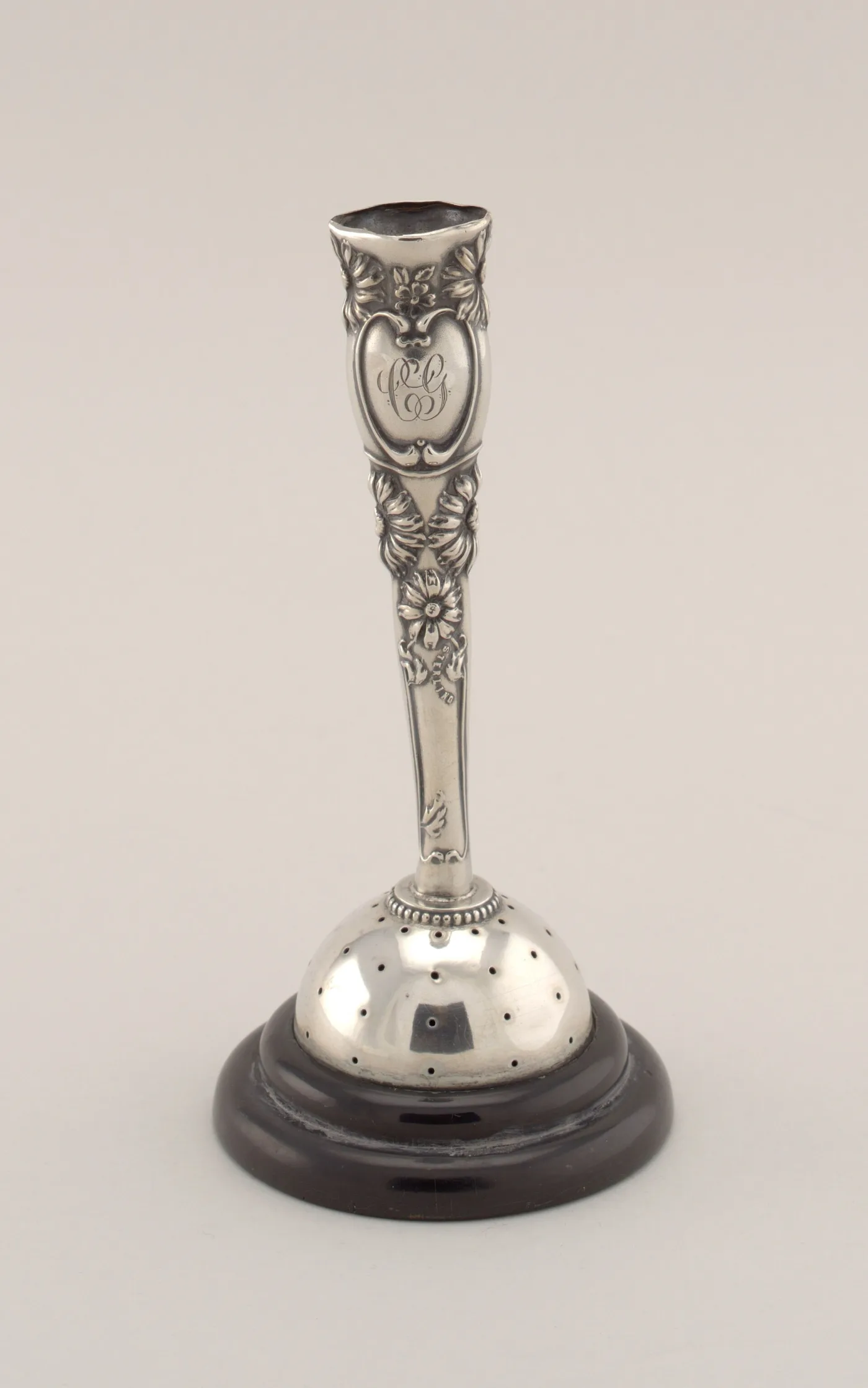 Silver hat pin holder: a pierced dome of small holes on a slender repoussé stem with an engraved monogram, standing on a dark turned wooden base