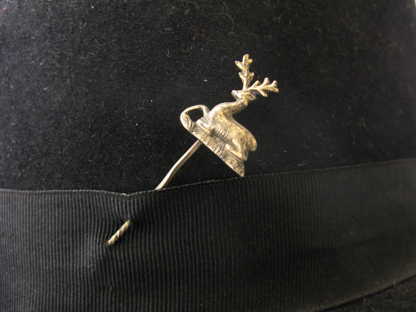 Gold-coloured stag hat pin pushed through the black felt crown and grosgrain band of a woman's bowler hat, its shaft re-emerging below the ribbon