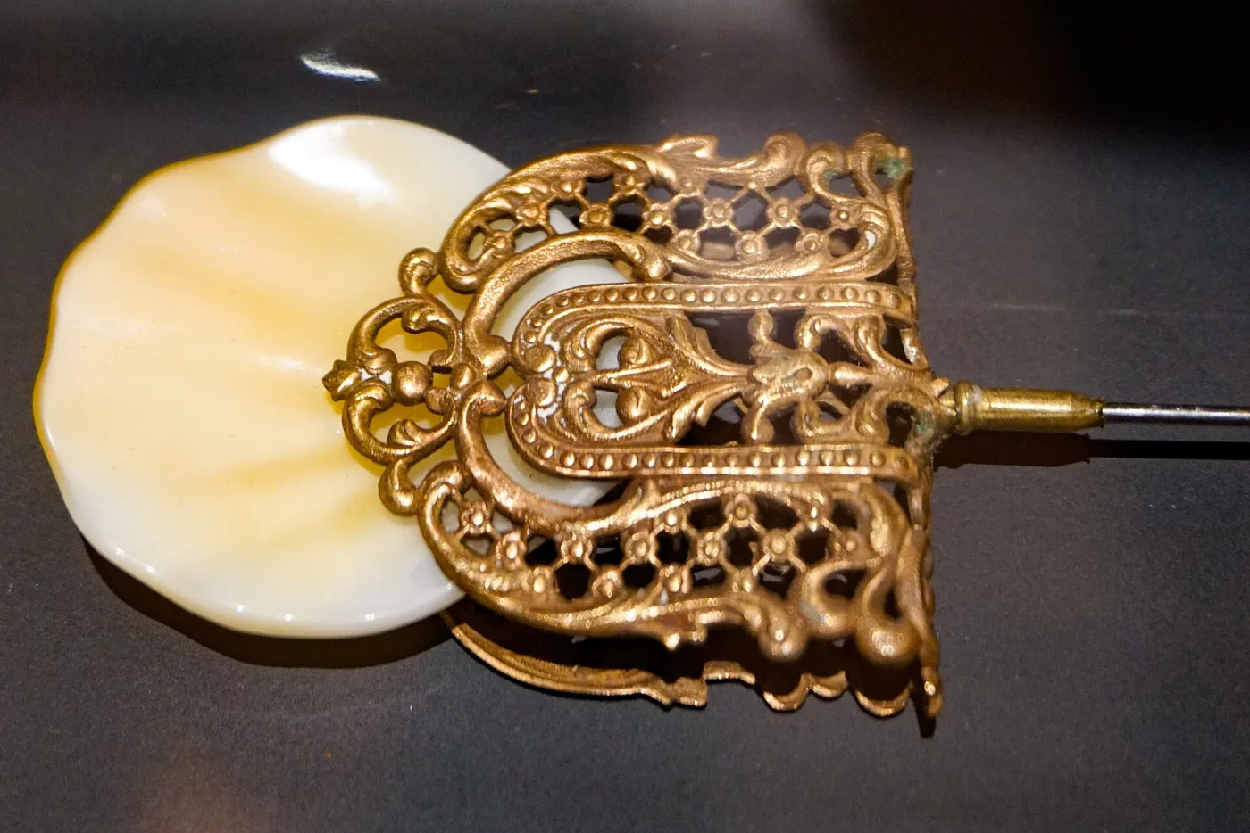 Large pierced gilt metal hat pin head of scrolling openwork laid over a cream glass disc, on a steel shaft