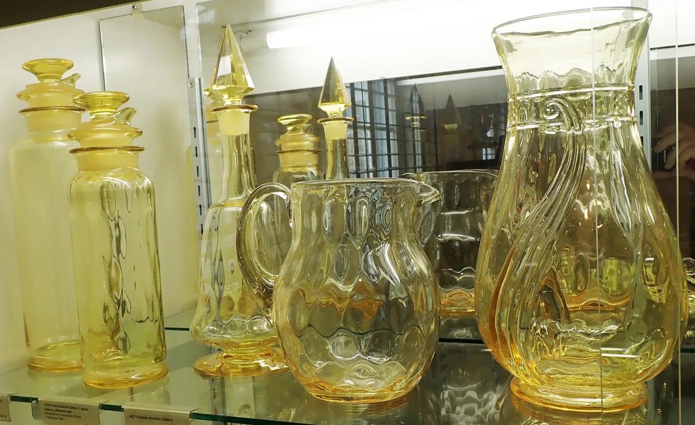Museum case of golden-yellow glass: covered jars with pointed finials, a jug and a tall pitcher
