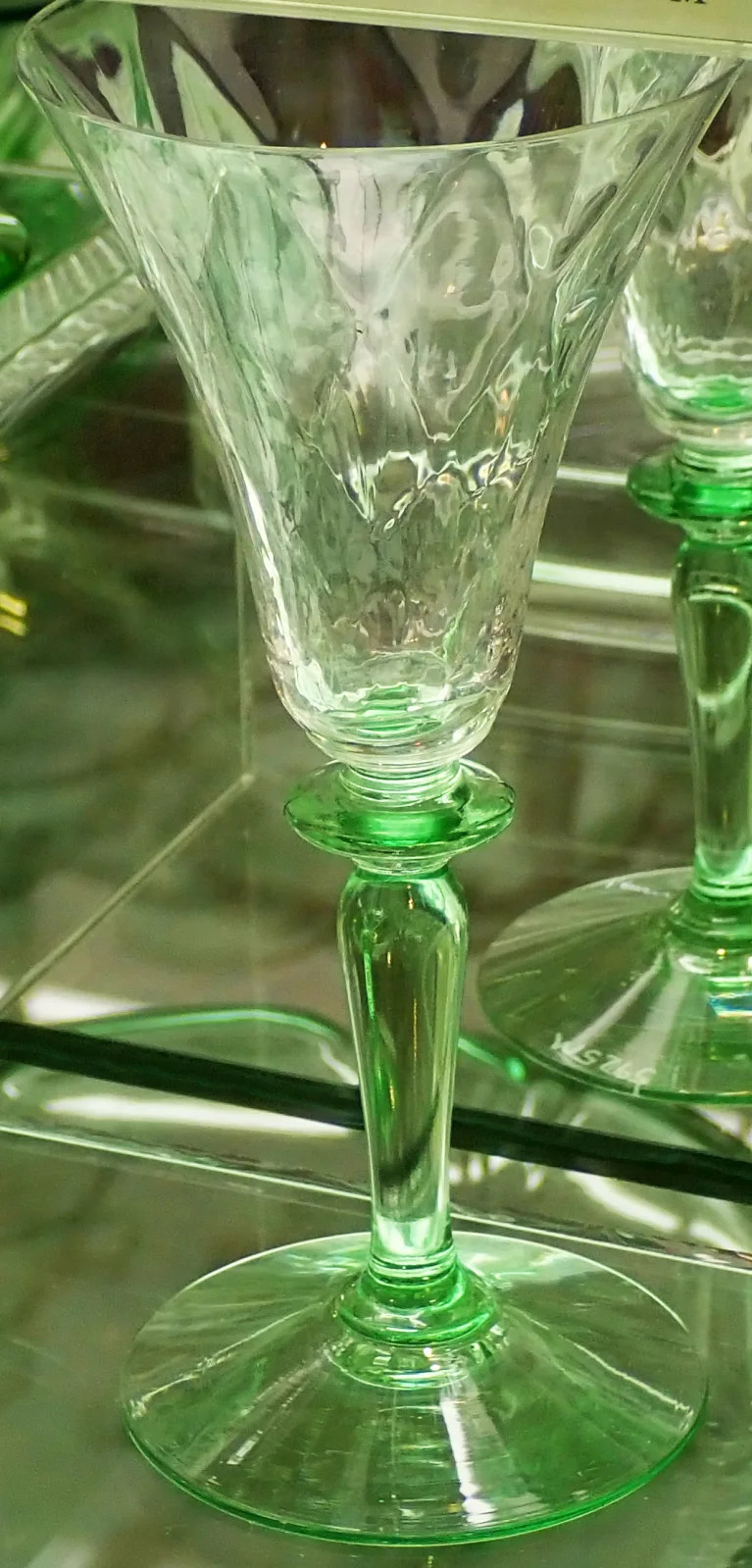 Wine glass with a clear bowl showing a diamond optic, set on a green stem and green foot with a flat green button below the bowl
