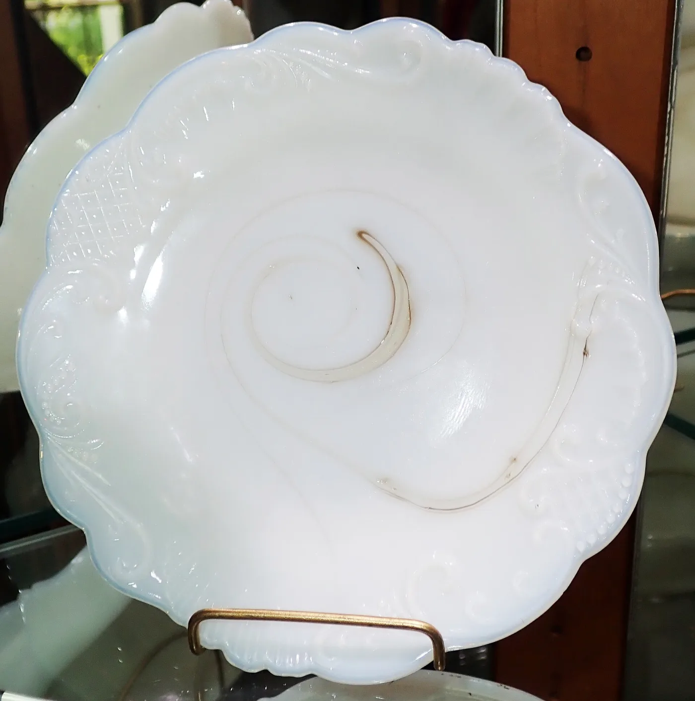 Opaque white glass plate with an embossed scrolled border and a swirled centre, on a wire stand
