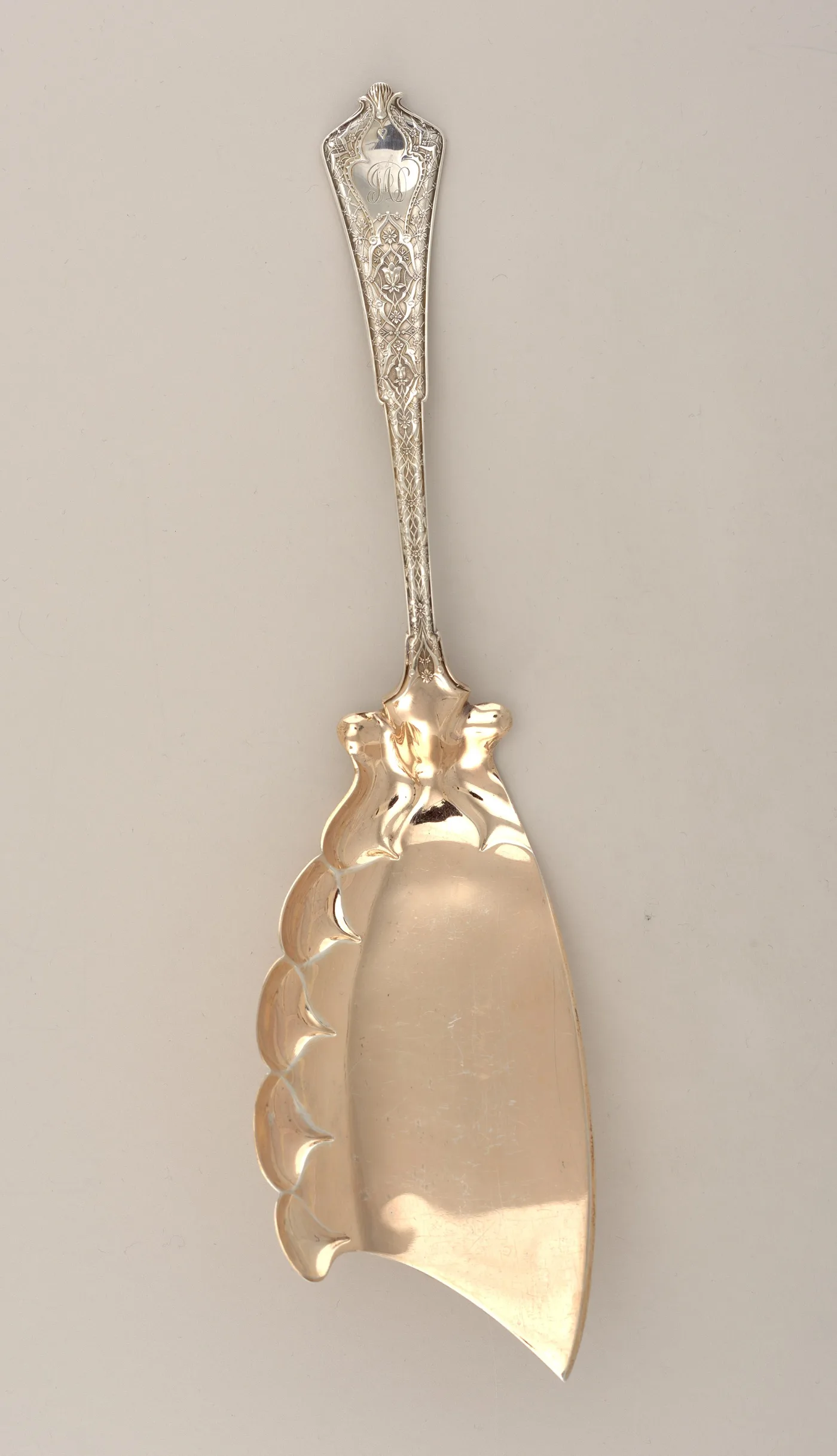 Gilded silver ice cream knife with an asymmetric lobed blade ending in a point, a pierced stem and a flat engraved handle