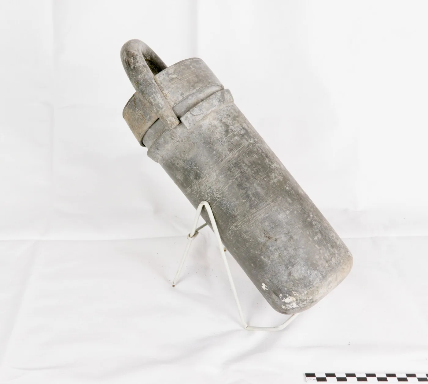 Cylindrical sorbet mould in solid pewter with a stepped slip-on lid and a heavy loop handle, resting on a wire stand with a photographic scale