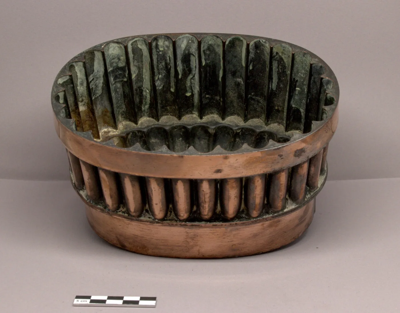 Looking into an oval copper mould, the deep fluted lining blackened and streaked where the tin coating has broken down, with bright copper at the rim