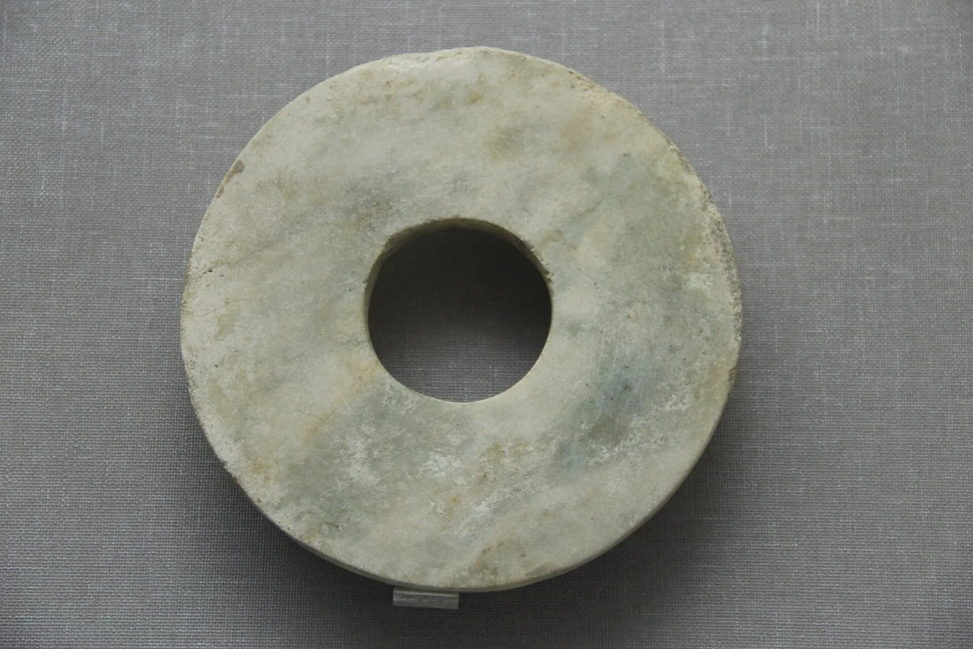 Stone disc with a central hole whose surface is chalky cream-white, patchier and more opaque around the rim than at the centre