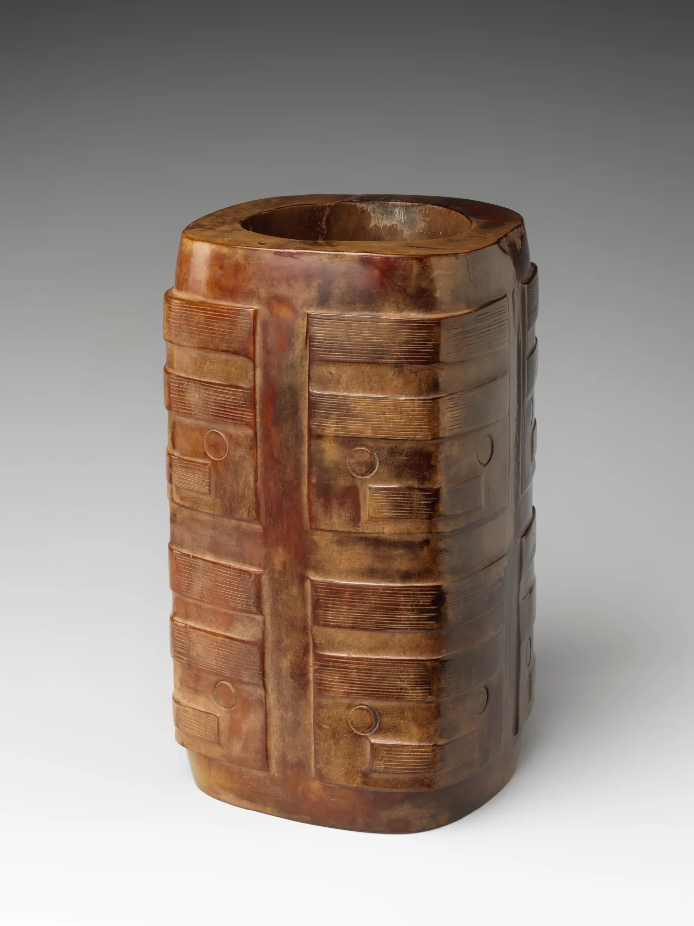 Squared tube of caramel-brown stone with a round bore, cut with crisp evenly spaced tiers and small raised discs