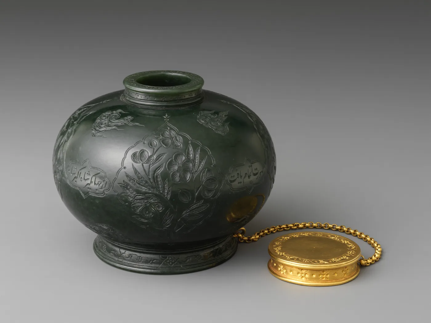 Squat dark green jade inkpot carved with flowering plants and Persian inscriptions in lobed panels, a gold lid on a chain beside it