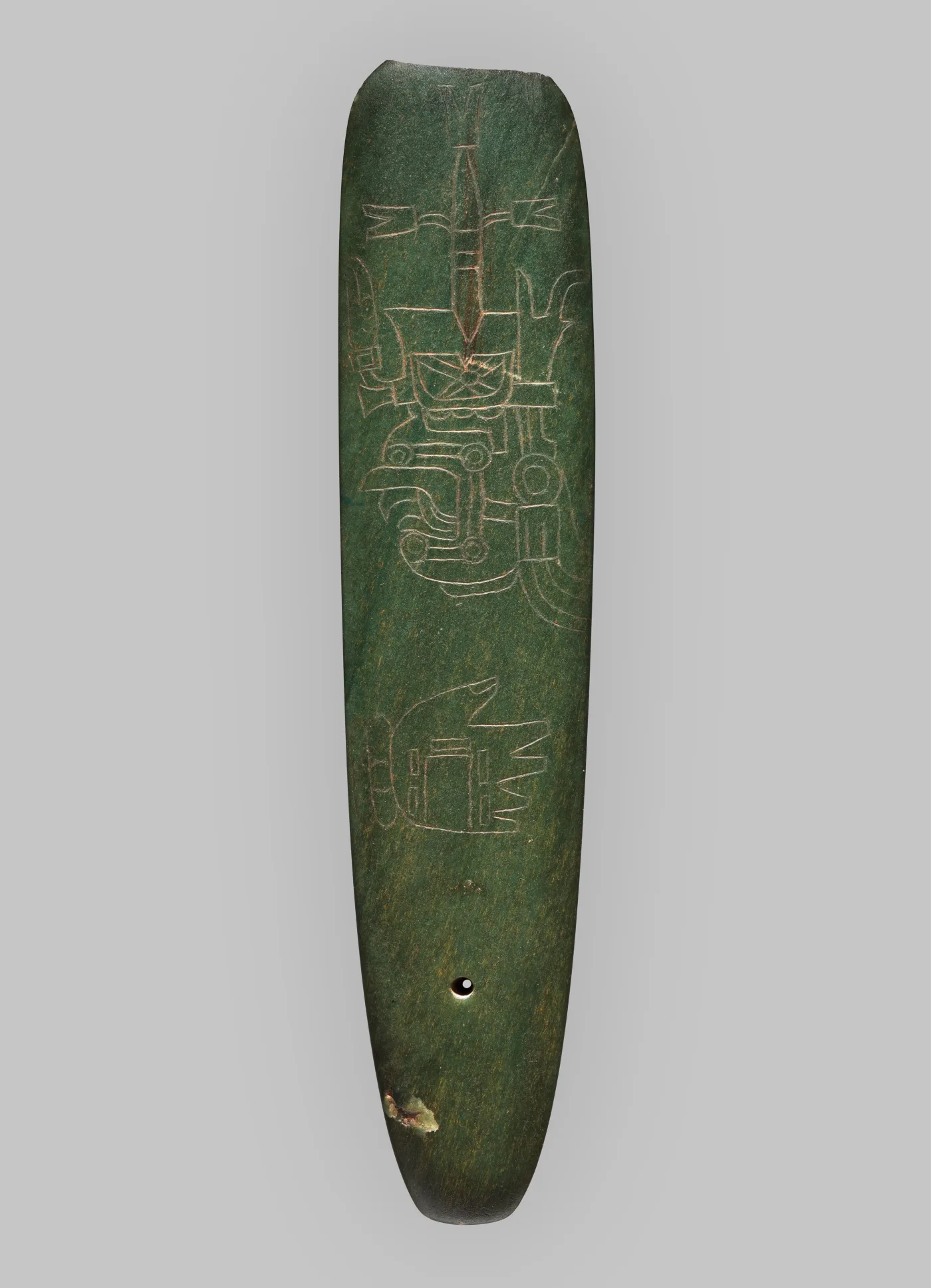Long narrow blue-green stone celt with a rounded cutting edge, its face incised with fine linear faces and motifs, a small drilled hole near the base