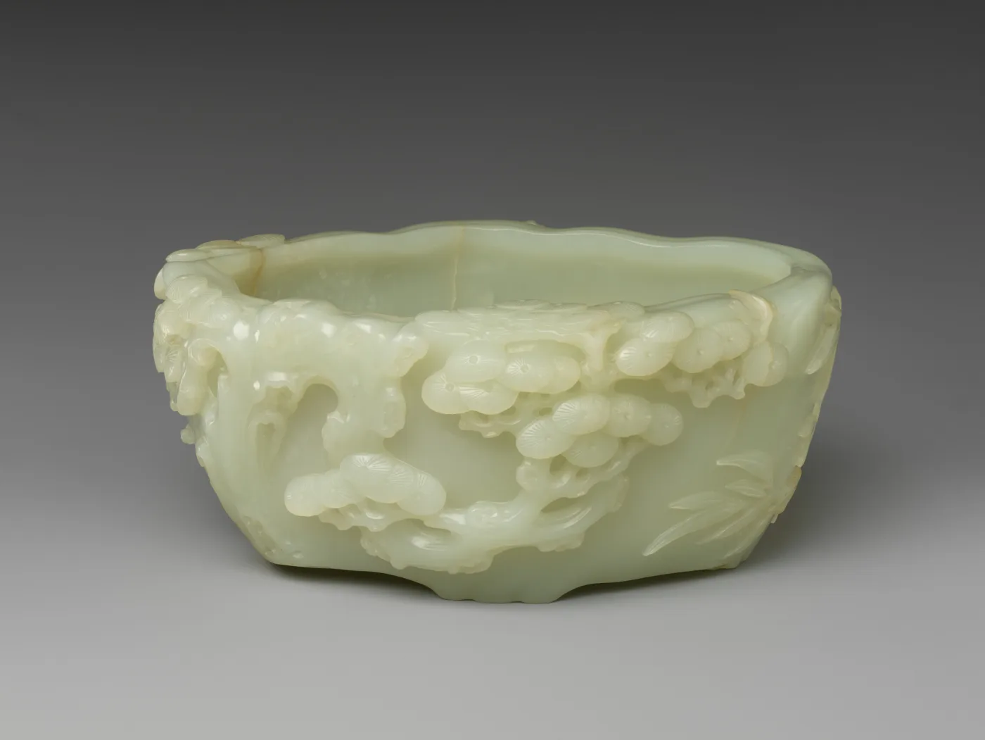 Shallow pale celadon jade brush washer, its outside carved in relief with a gnarled pine trunk and clusters of needles