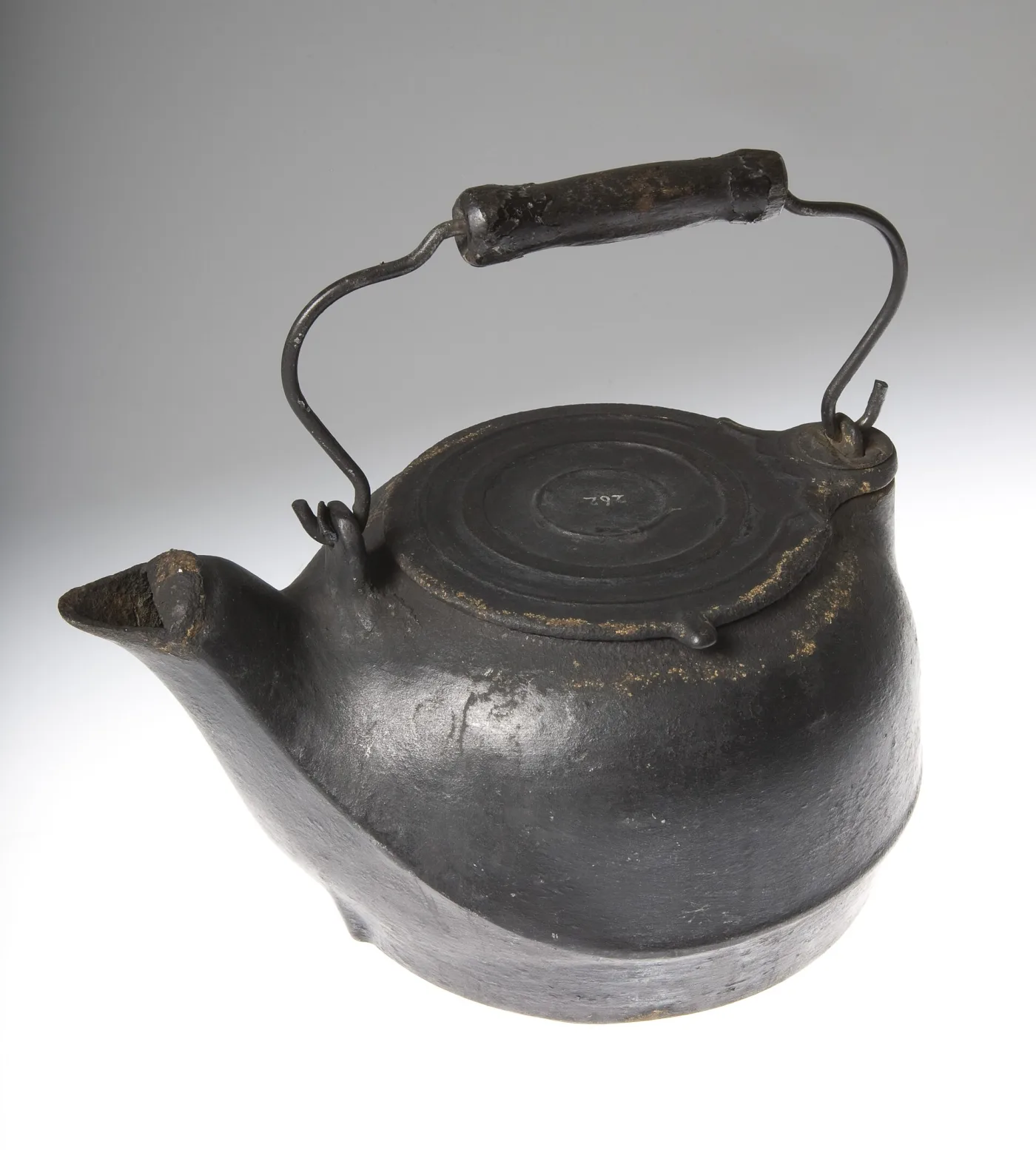 Black cast iron kettle with a squat body, short gooseneck spout, recessed lid and a wire bail handle with a turned wooden grip