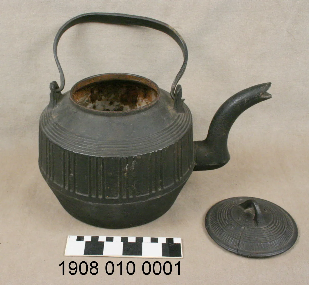 Grey cast iron kettle with its domed lid lifted off and set beside it, showing a rusted interior rim and vertical ribbed casting on the body