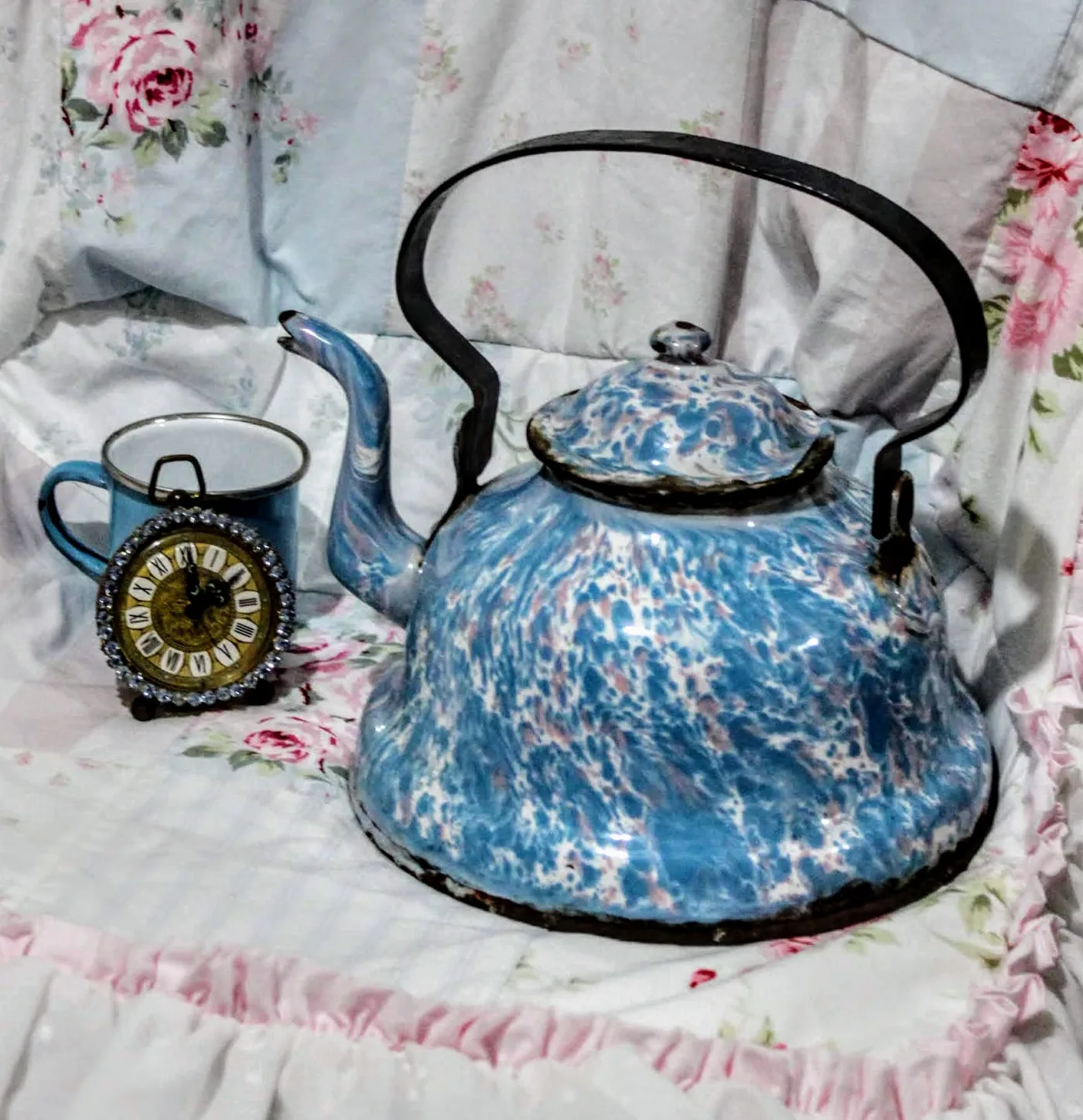 Blue and white swirl-patterned enamelware kettle with a black iron bail handle, chipped around the rim and base