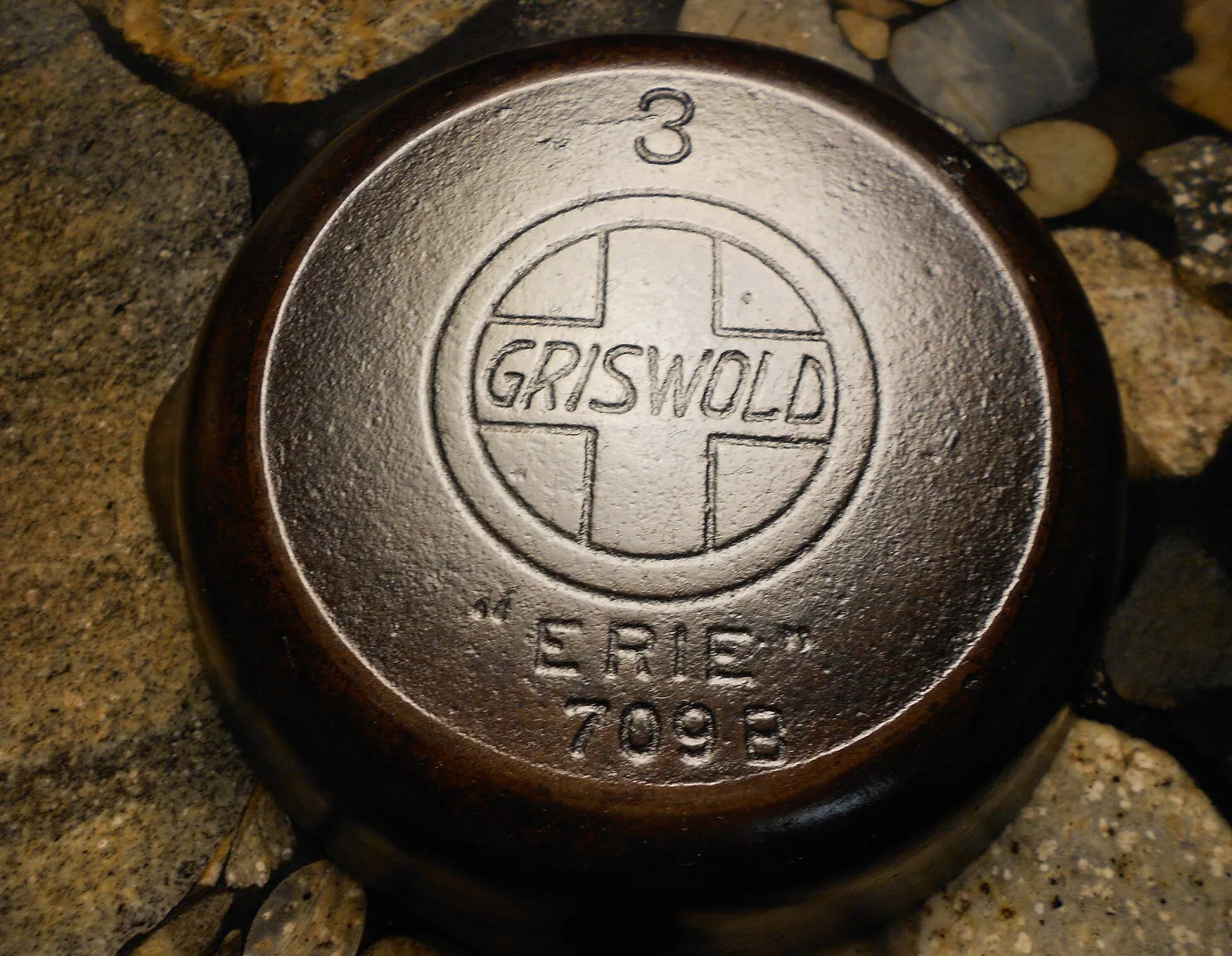 Underside of a cast iron pan cast with a large circled cross trademark lettered GRISWOLD, with ERIE and a pattern number below