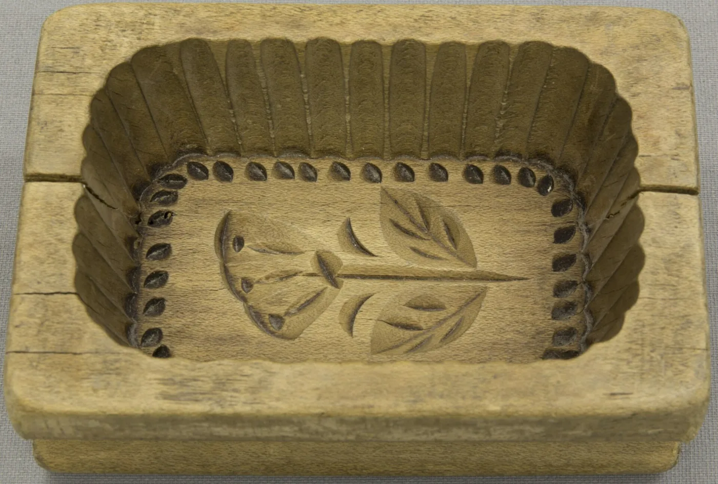 Rectangular carved wooden butter mould shaped as an open box, the inside of its base cut with a leafy spray and the walls with a row of scalloped notches