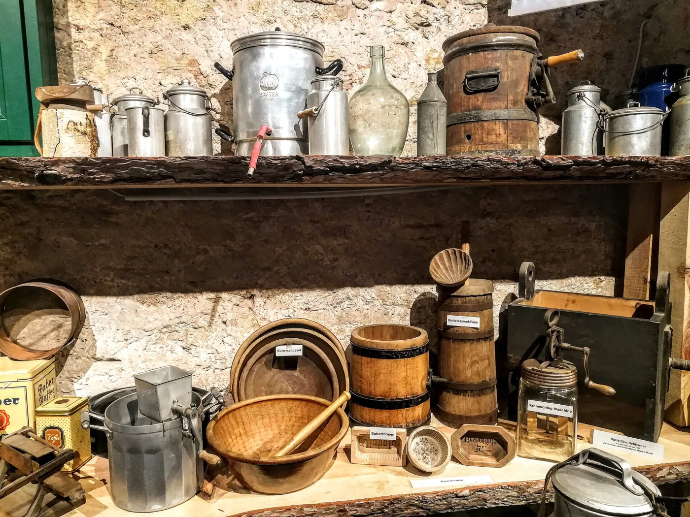 Museum display of wooden dairy equipment, including a tall staved butter churn, several carved butter moulds, shallow wooden bowls and a cream-whisking machine, arranged on a table