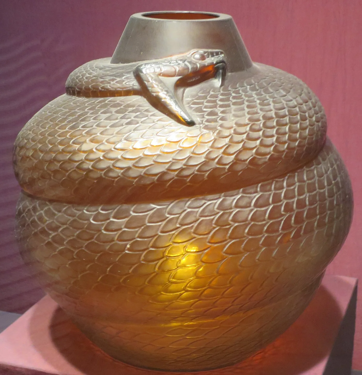 Squat spherical vase entirely covered in moulded scale pattern, with a snake modelled in the round coiling around the shoulder and its head raised at the rim, the glass a warm amber