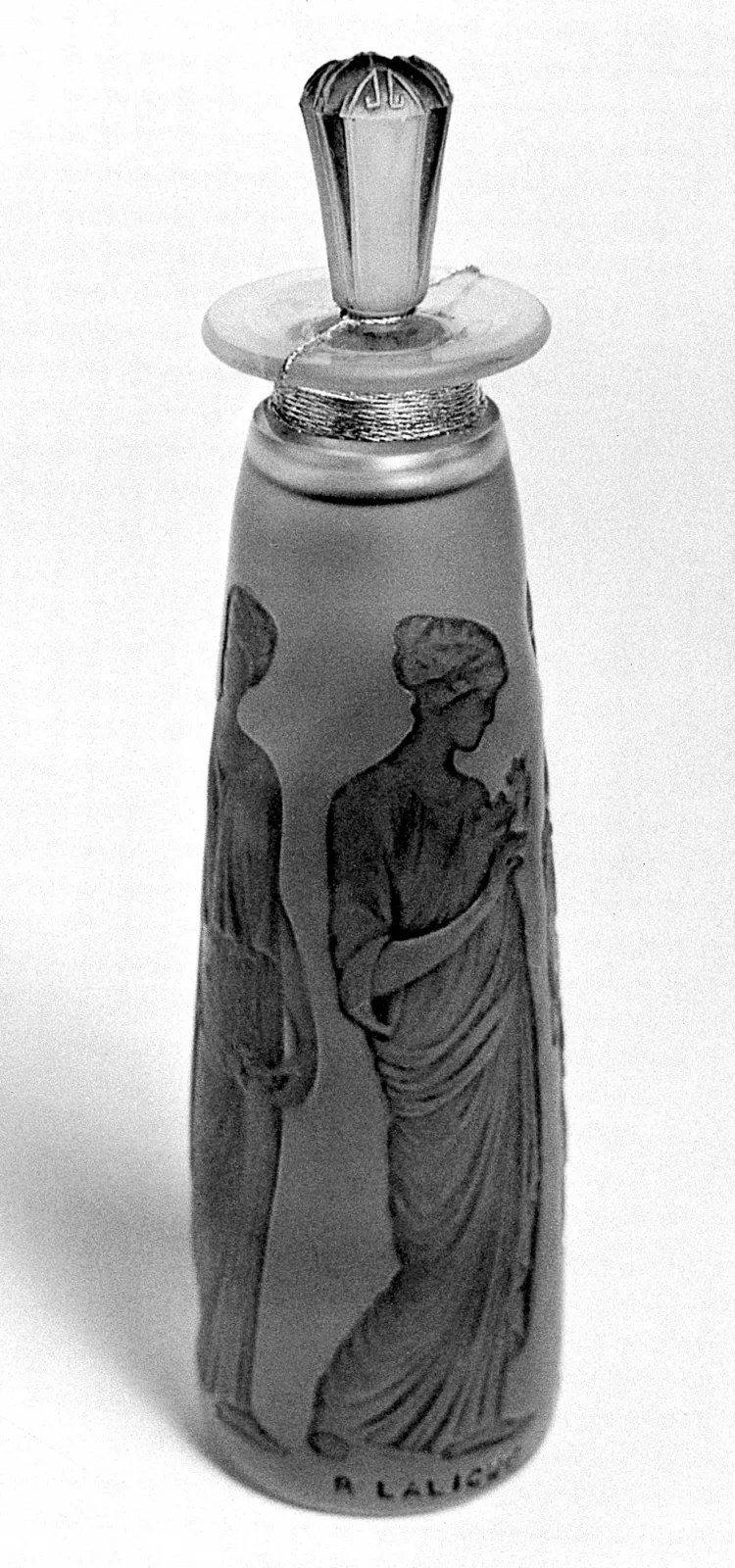 Tall cylindrical frosted glass scent bottle moulded with classical draped figures in relief, with a domed clear stopper, photographed in black and white against a plain ground