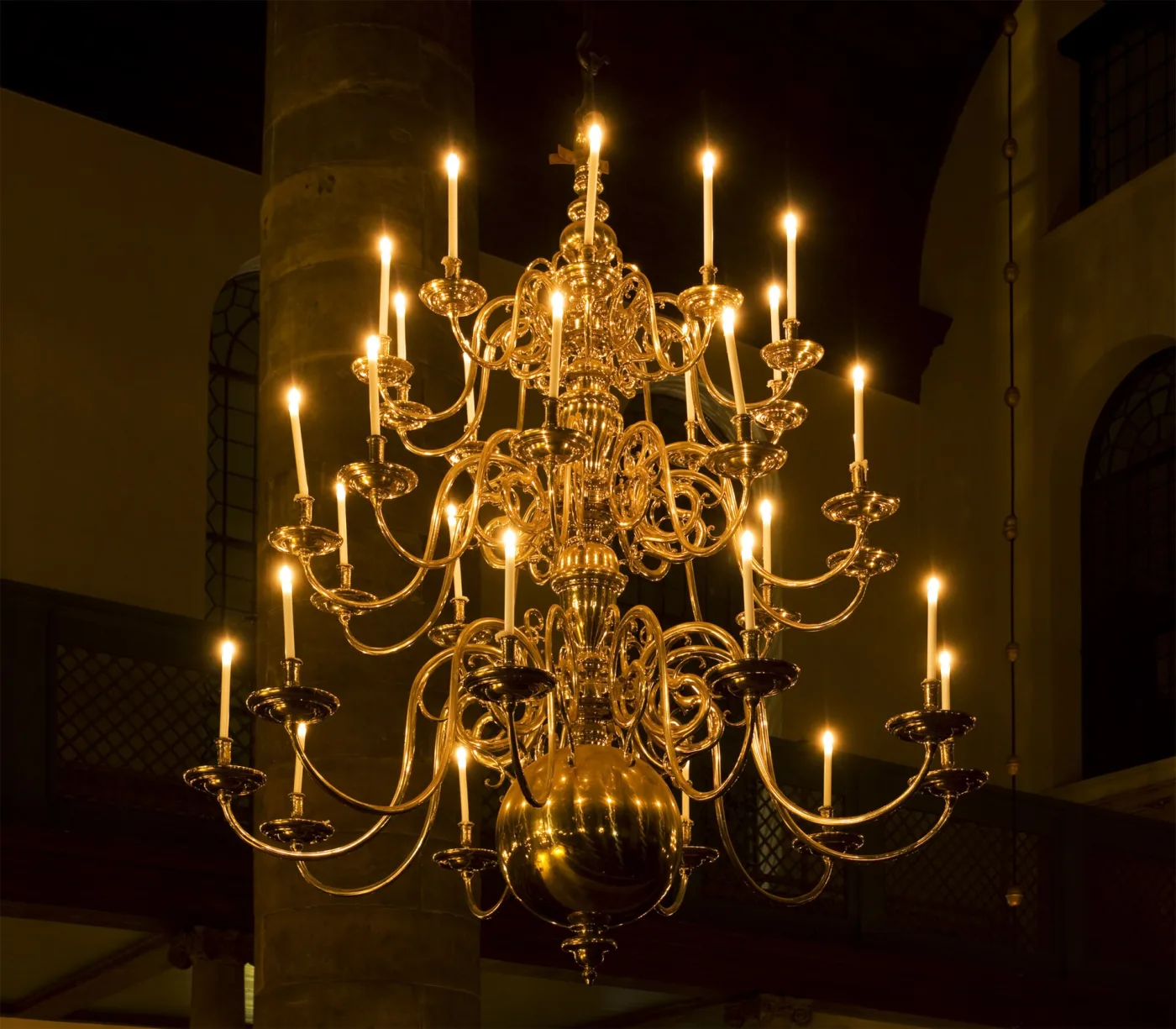 Large brass chandelier of many tiers of scrolled arms hanging in the Esnoga synagogue in Amsterdam, every arm holding a lit candle