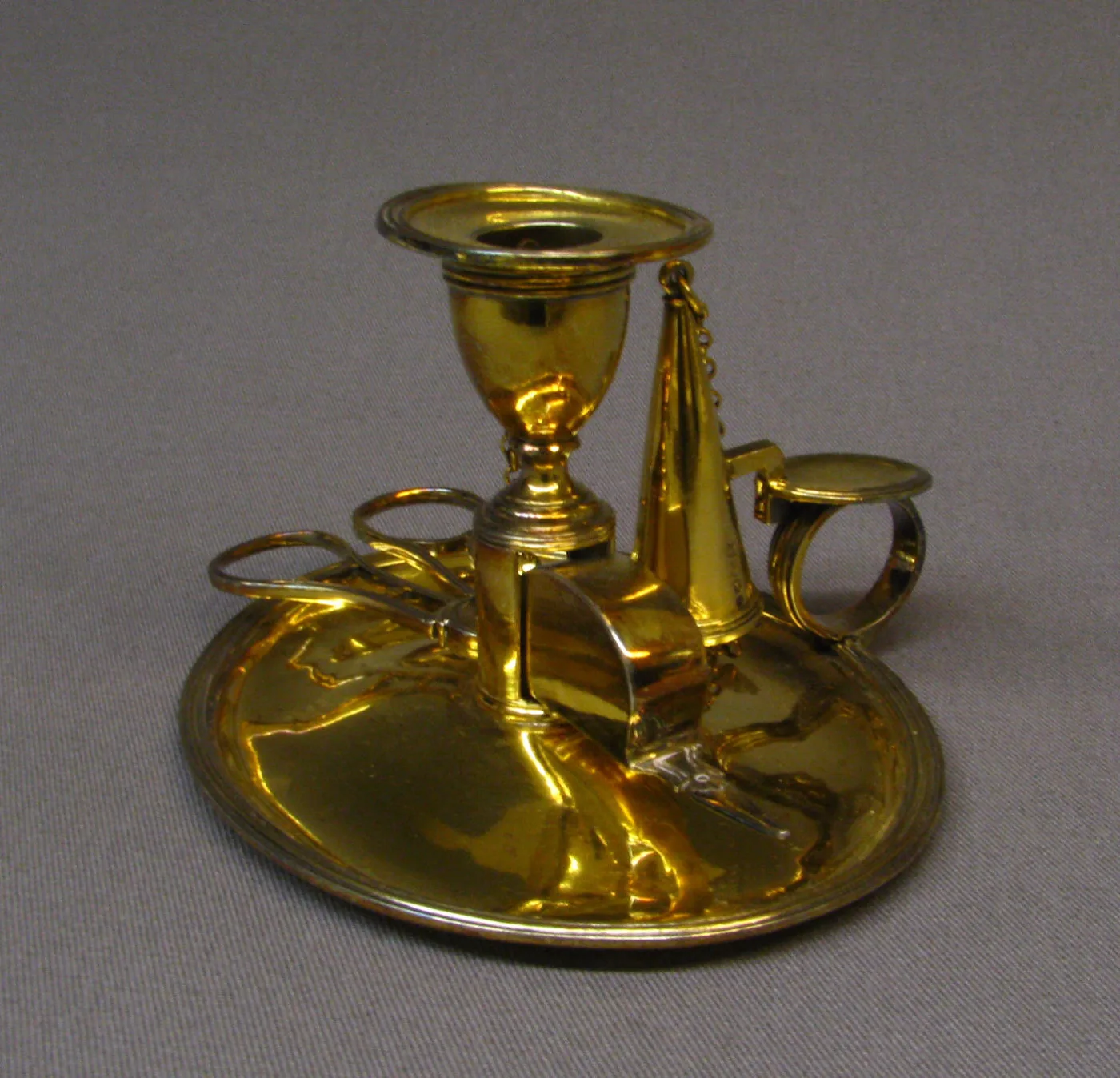 Silver gilt chamber candlestick of 1801 to 2 by John Emes with a baluster socket, a circular dished pan, a ring handle, a conical extinguisher hooked beside the socket and a pair of scissor snuffers lying across the pan