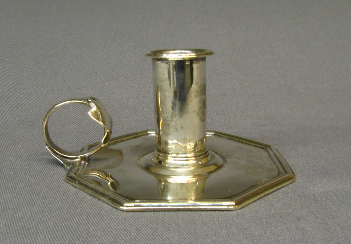 Plain silver chamber candlestick of about 1670 to 1680, a cylindrical socket on an octagonal dished pan with a moulded rim and a wire ring handle