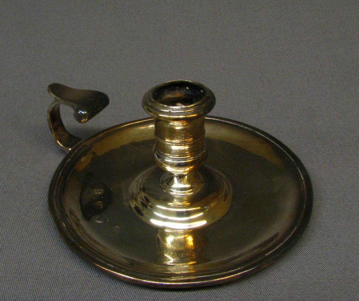 Plain silver chamber candlestick of 1714 to 15 by Joseph Bird with a baluster socket on a broad dished pan and a flying scroll handle