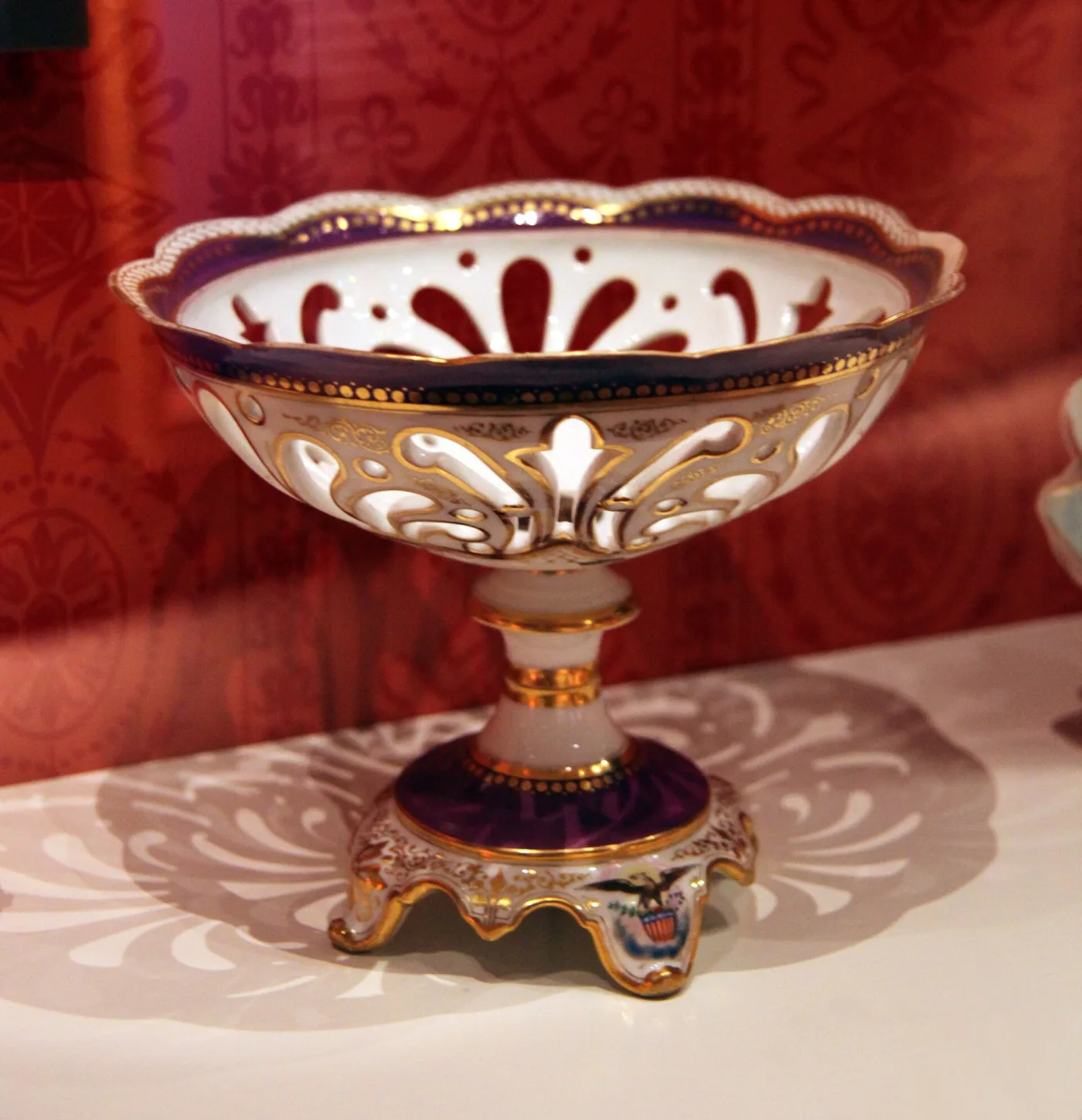 Footed porcelain compote dish with a pierced rim, a purple-red and gold border, and the American eagle and shield painted in the centre