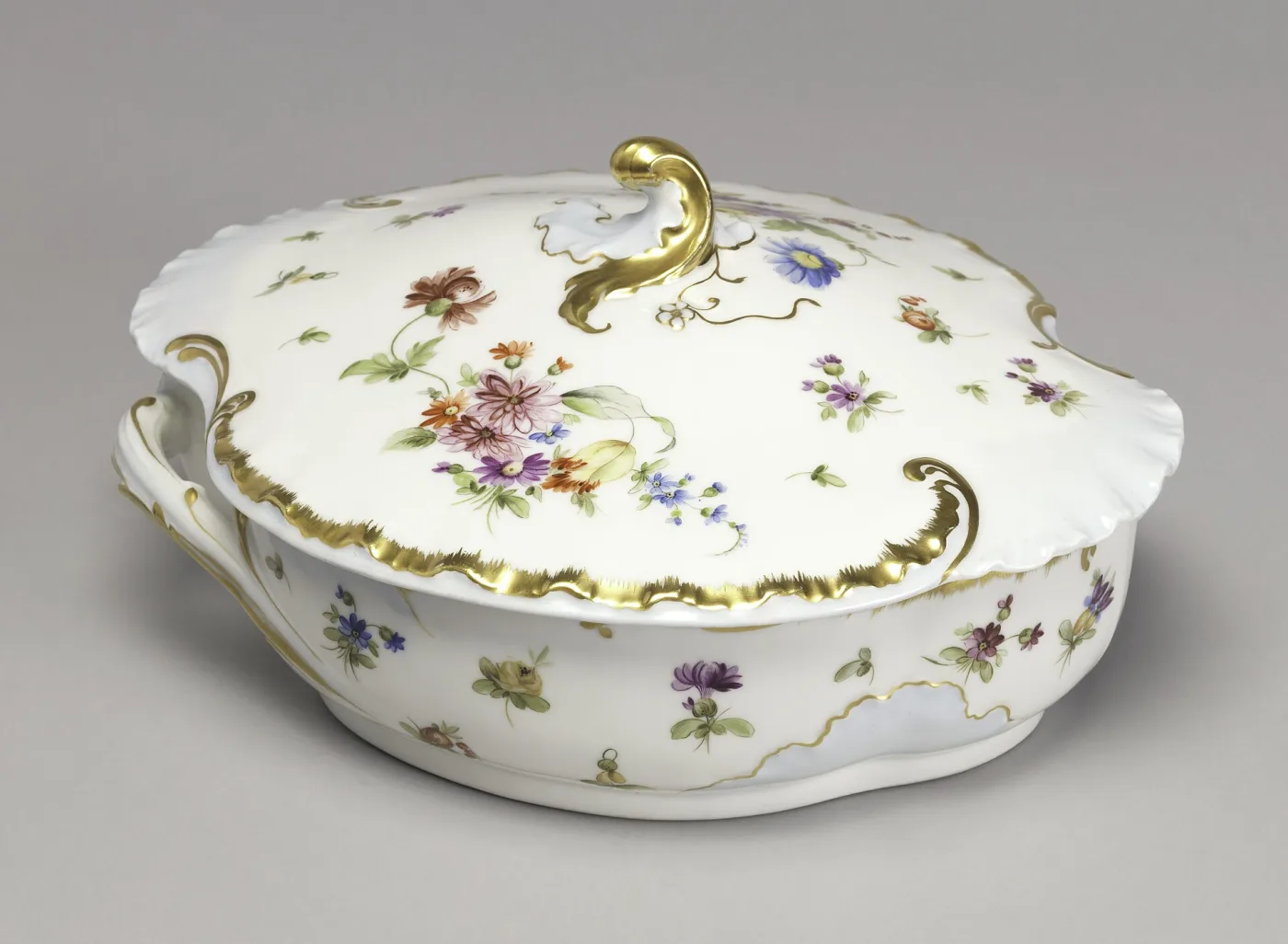 White porcelain covered vegetable dish with two handles and a gilt finial, painted with floral sprays and gilded rococo borders over pale blue panels