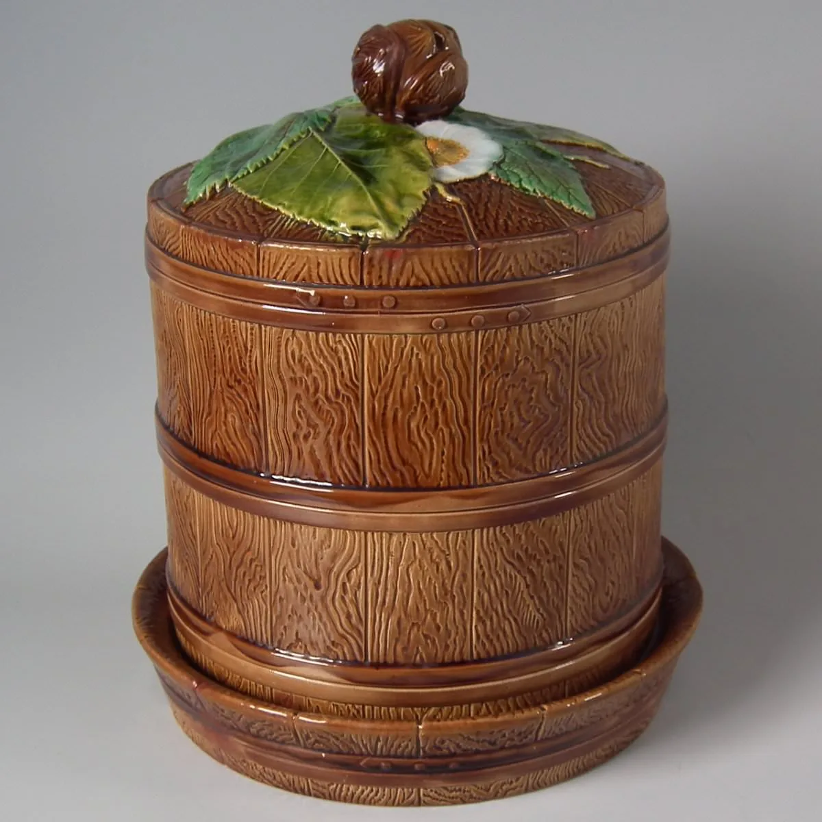Cylindrical covered dish and stand glazed to imitate a wooden barrel with basketweave banding, the lid topped by a modelled chestnut and green leaves
