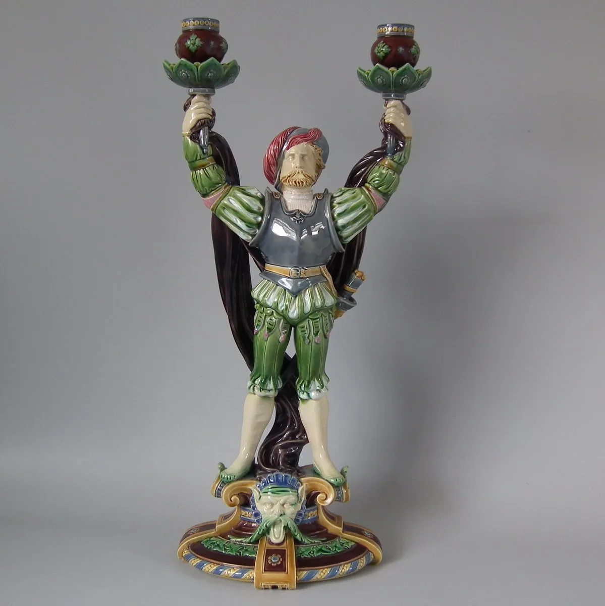 Candelabra modelled as a standing figure in Renaissance dress and armour holding up two foliate candle nozzles, on a decorated plinth with a mask below