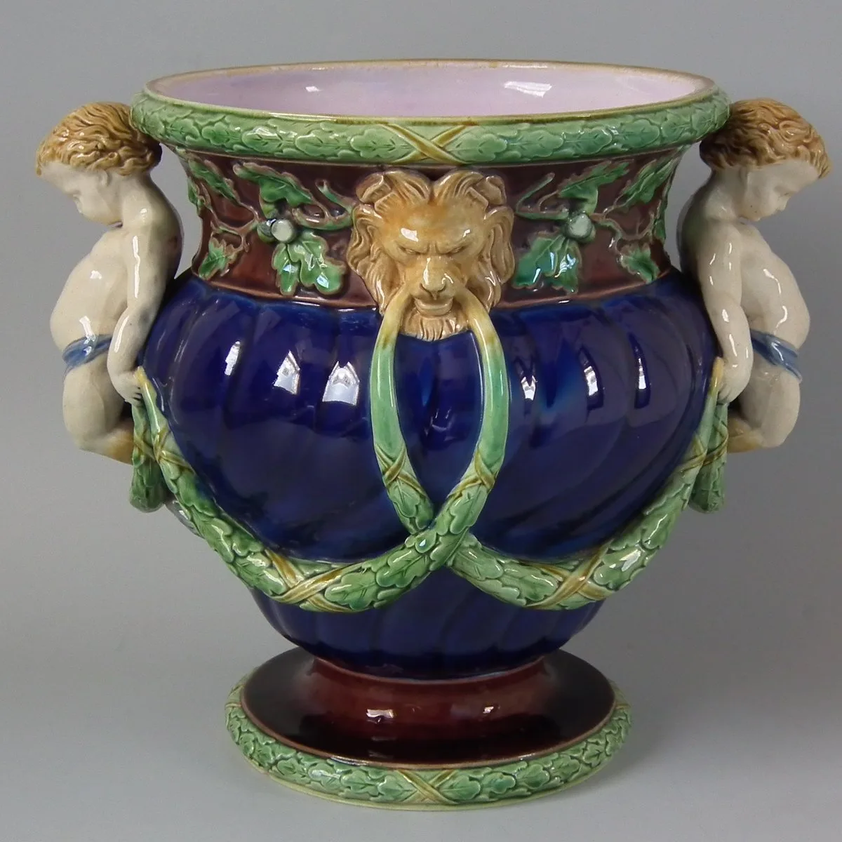 Deep cobalt-blue jardiniere with a lion mask on the body, garlands of oak leaves and acorns, and two faun figures modelled in relief at the sides, on a pink-lined rim and dark red foot