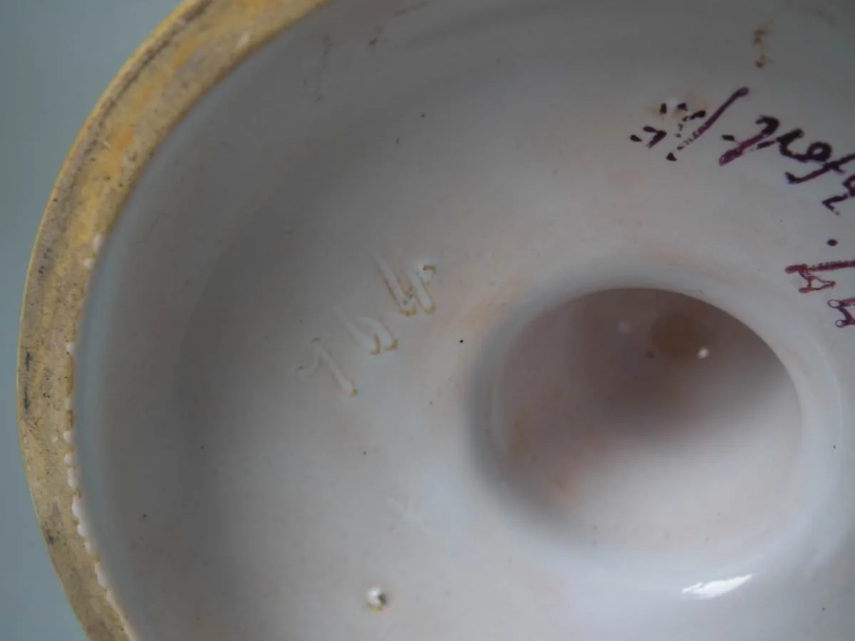 Underside of a majolica dish showing a plain cream tin glaze with a painted date cypher and a brush-written signature in dark pigment