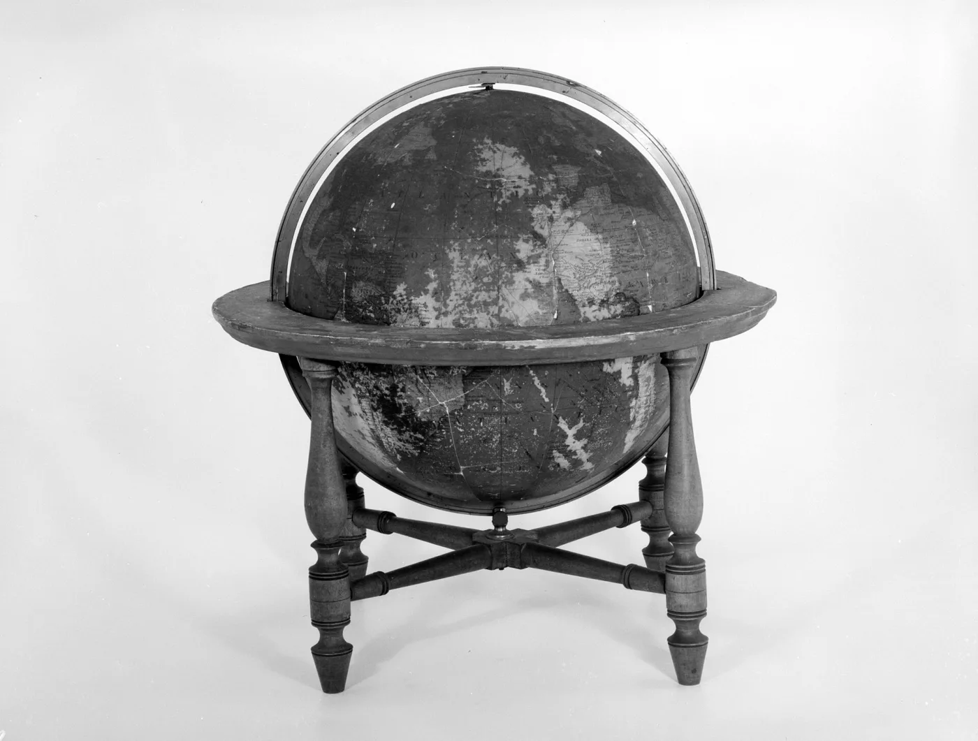 Celestial globe in a wooden stand with a horizontal ring, its dark surface covered in constellation figures and stars, photographed in black and white against a plain ground