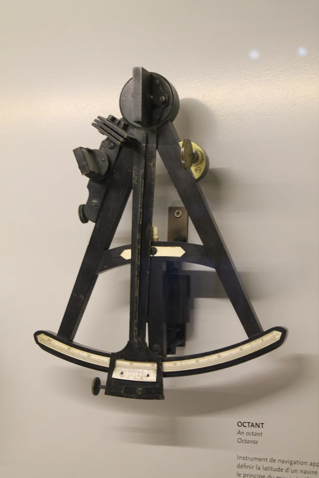 Octant with a dark wooden triangular frame, ivory scale along the arc, a brass index arm and small mirrors and shade glasses mounted on the upper limb