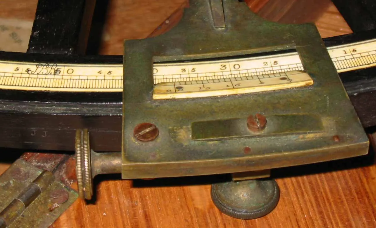 Close view of an octant's inlaid ivory scale graduated in degrees, with the brass index arm and its vernier scale crossing it, and a small stamped mark visible on the arc beyond