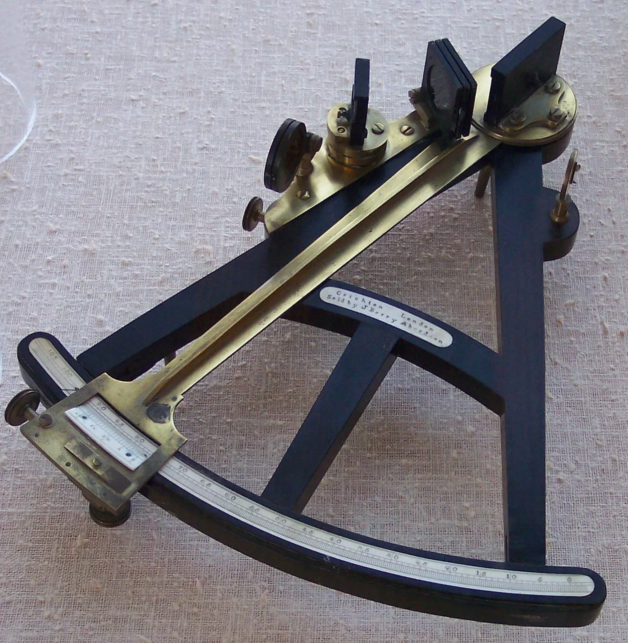 Octant with a black wooden A-shaped frame, a long brass index arm pivoting at the apex, an inlaid ivory scale along the curved arc and a small ivory maker's label on the crossbar, standing on three feet