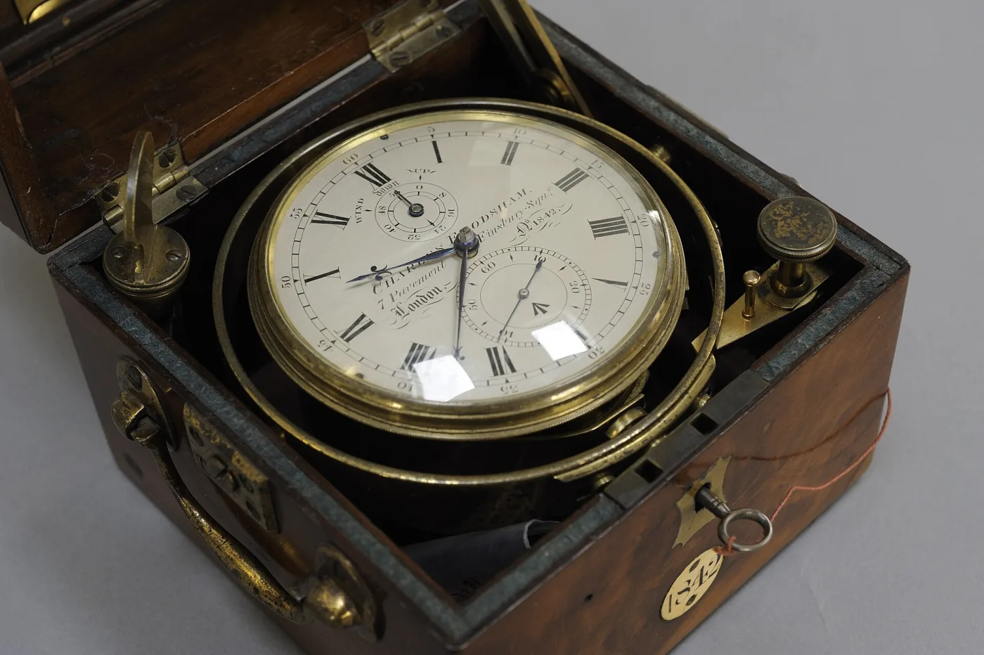 Marine chronometer with a white enamel dial and subsidiary seconds, gimbal-mounted in a brass bowl inside a two-tier wooden box with a hinged lid