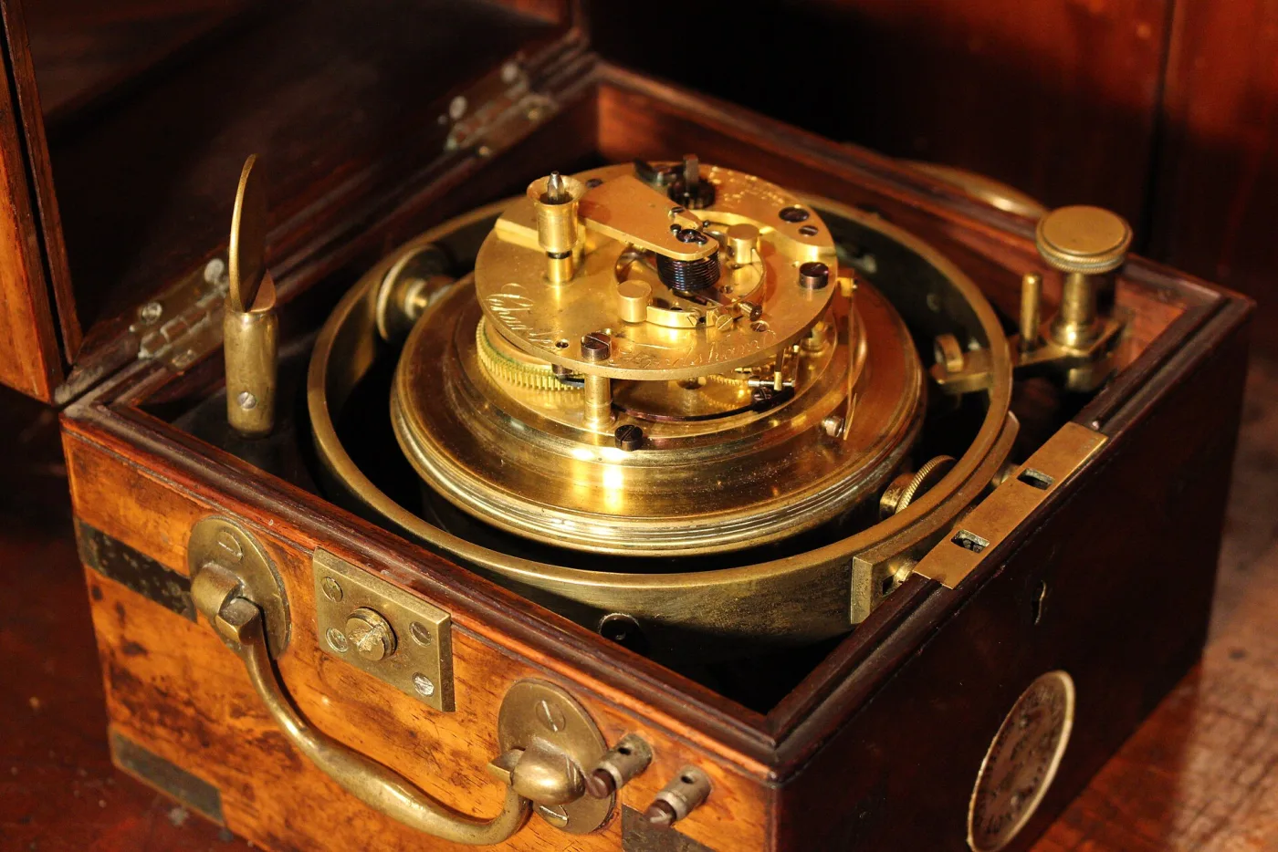 Marine chronometer movement seen from above, a heavy gilt drum in gimbal rings inside a mahogany box, showing the balance and the winding arrangement