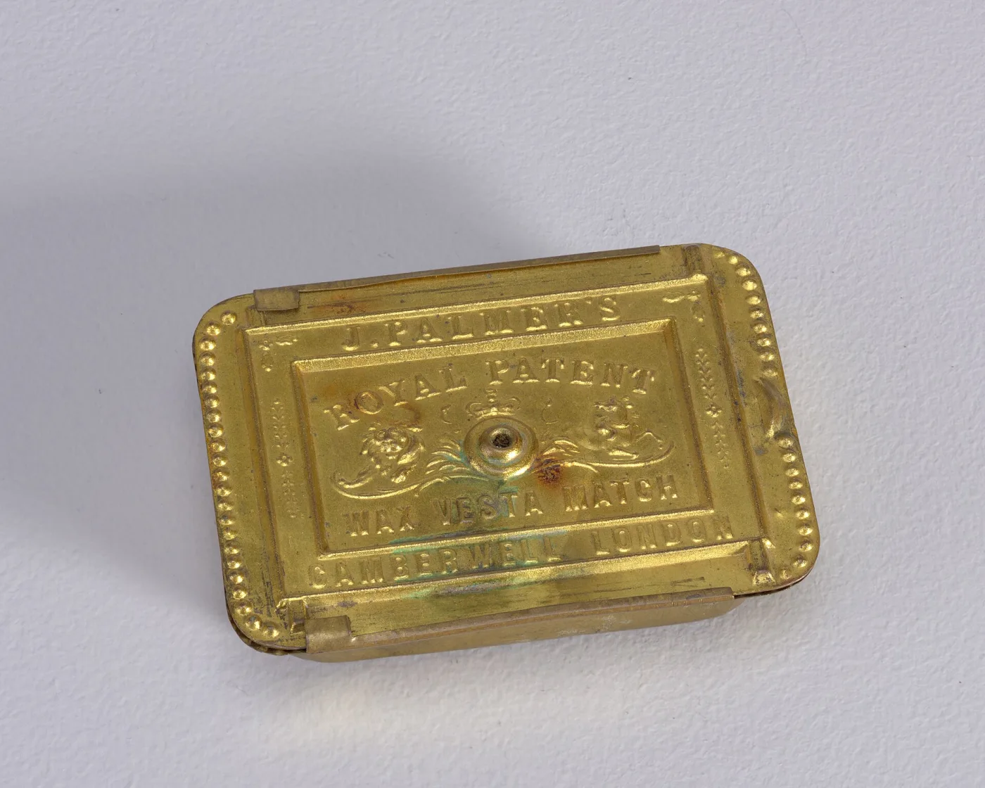 Small rectangular gilt-brass box with canted sides and beaded edges, its sliding lid stamped with a royal arms and an inscription naming a wax vesta match maker