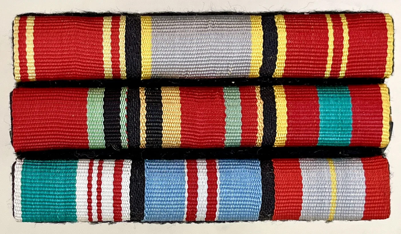 Three rows of ribbon bar mounted one above another, each made up of short lengths of striped ribbon in reds, blues, greens, yellow and white, stitched onto stiffened backing