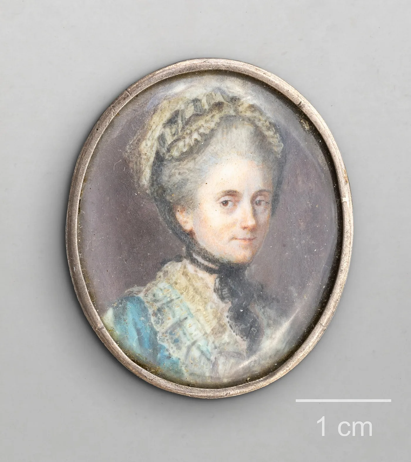 Oval portrait miniature of a woman in a lace cap, shown beside a one centimetre scale bar