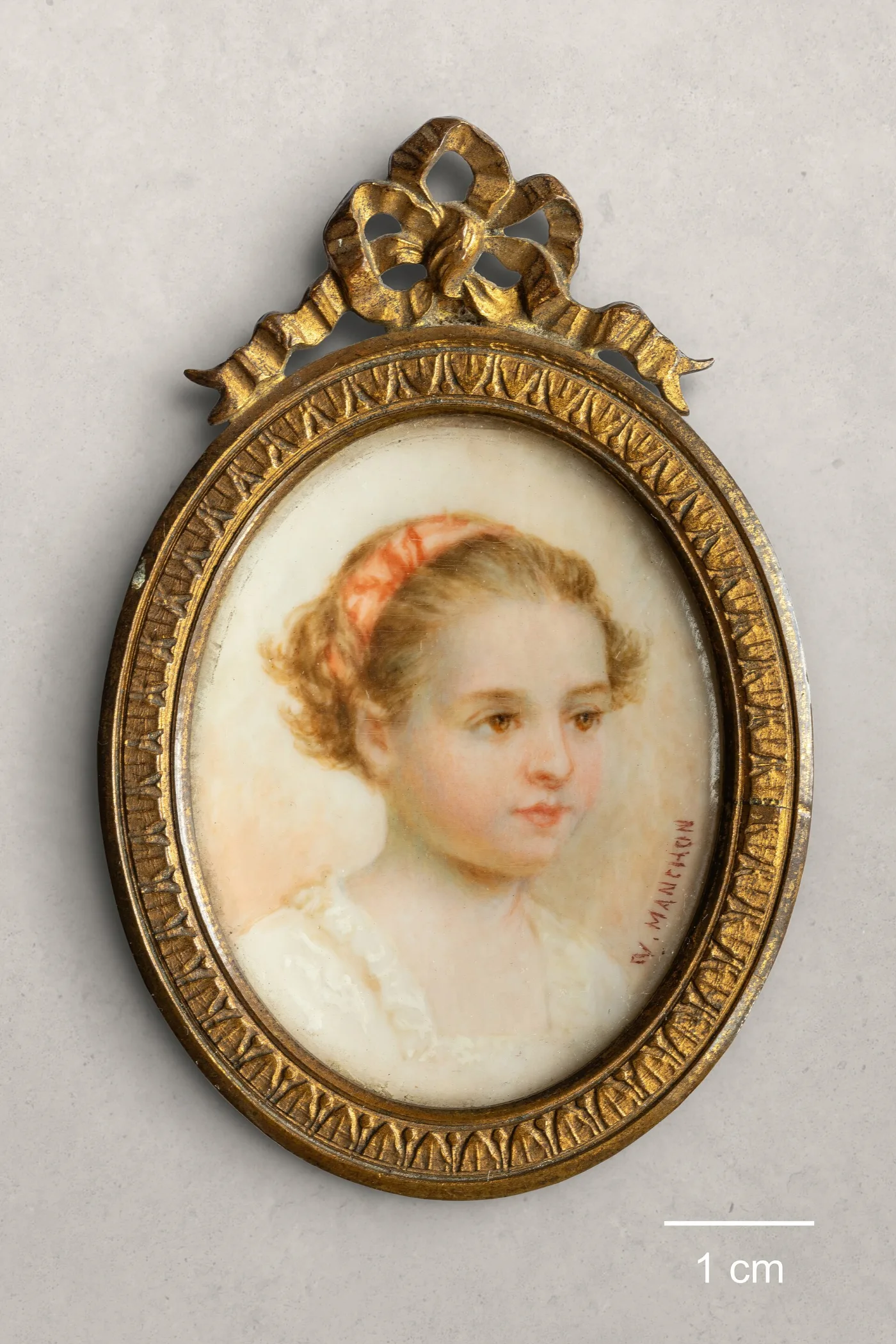Oval portrait miniature of a girl in a gilt frame with ribbon-bow cresting, beside a one centimetre scale