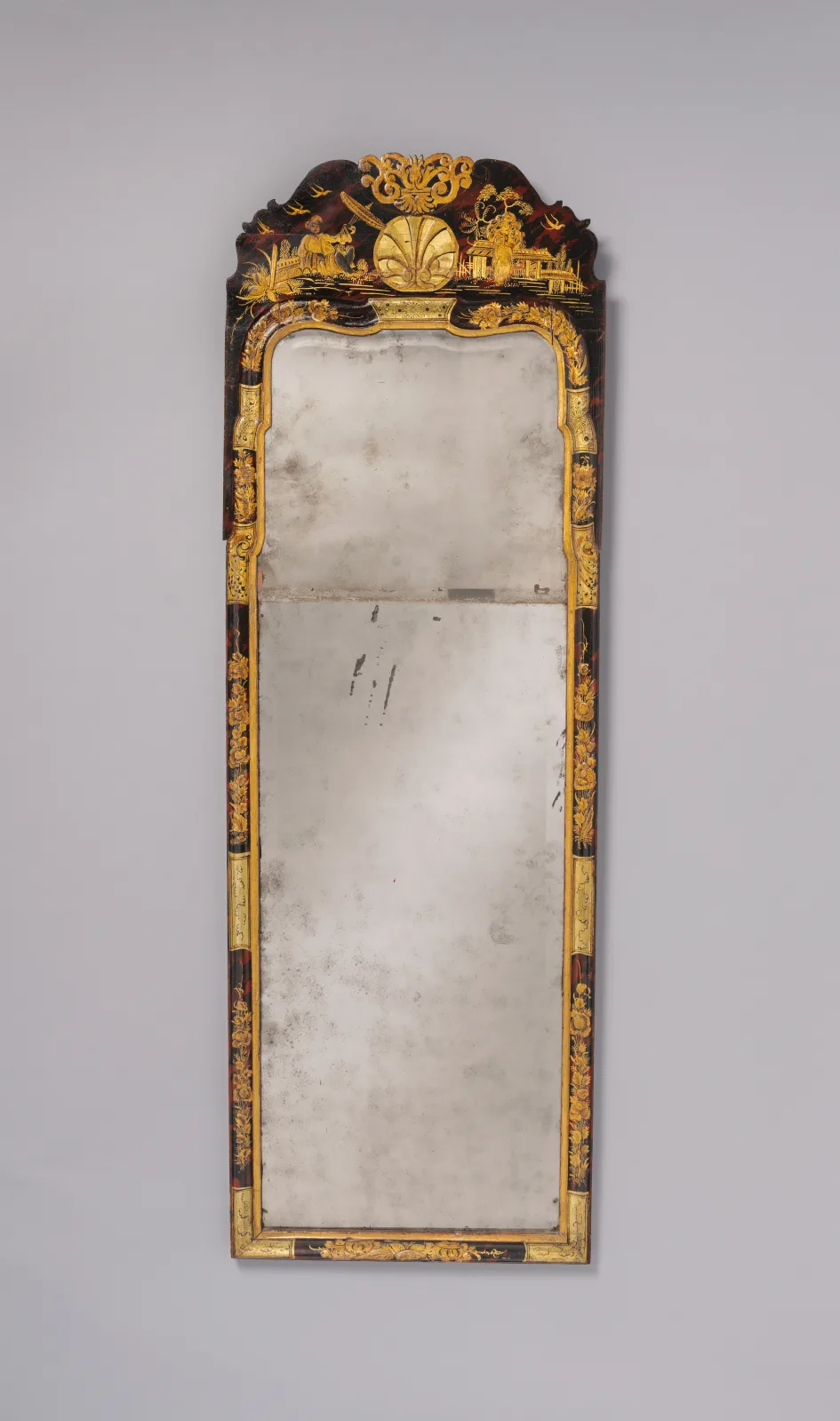 Tall narrow japanned looking glass with an arched gilt crest, its glass made of a short arched upper plate above a long rectangular lower plate