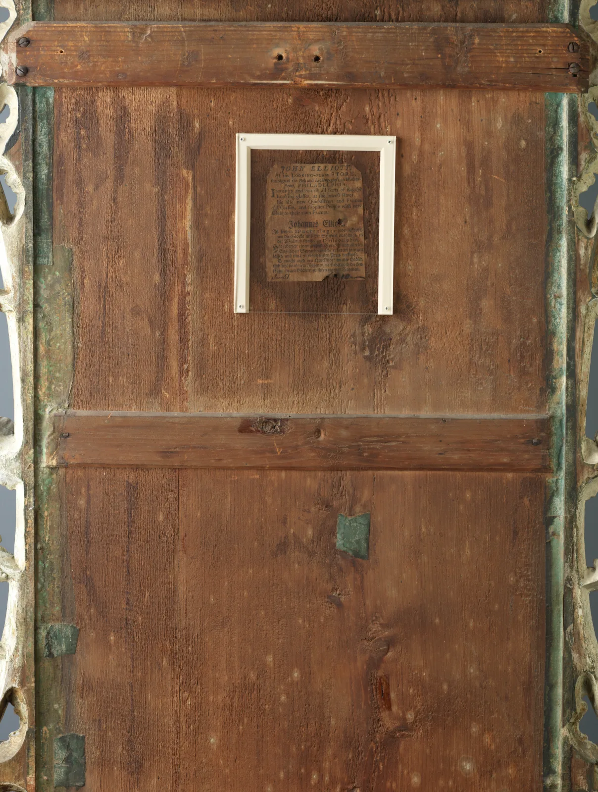 Back of a carved looking glass showing vertical wooden boards crossed by horizontal battens, with a framed paper label in the upper half